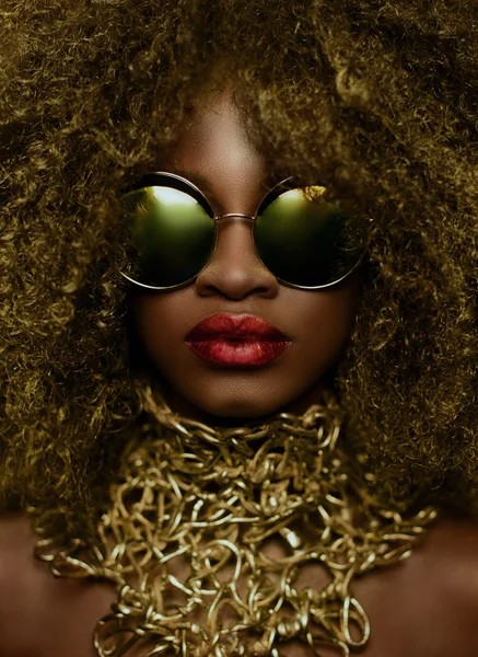 Close-up portrait of magic golden african american female model in massive sunglasses with bright glitter makeup, glossy hairstyle and big red lips. Studio shoot — Stock Photo, Image
