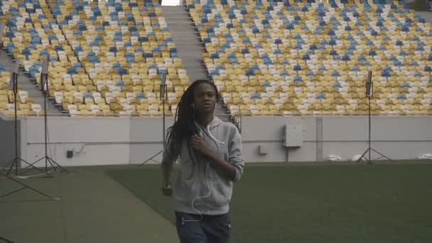 Joven sexy afroamericana en forma mujer escuchando música y trotando en el fondo del estadio urbano — Vídeos de Stock