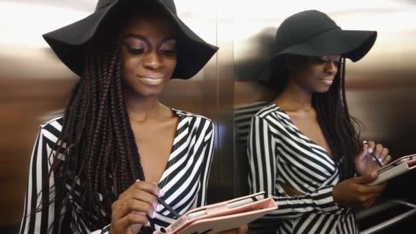 Elegante glamouröse afrikanisch-amerikanische Frau in einem gestreiften Cocktailkleid mit ihrem Tablet-Computer — Stockvideo