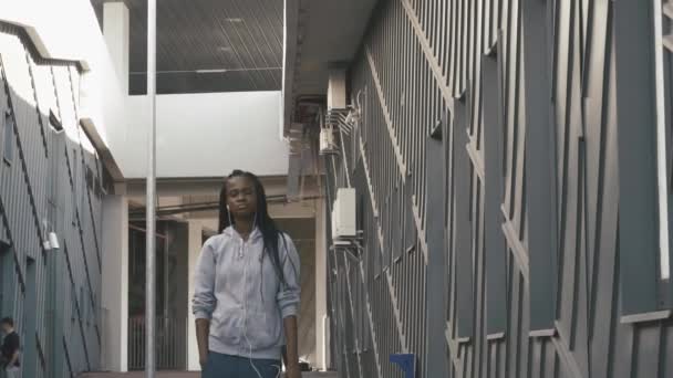Mladá sebevědomá promyšlené afroamerické žena s dredy chůzi a poslech hudby do sluchátek. Šedá textura městské pozadí — Stock video
