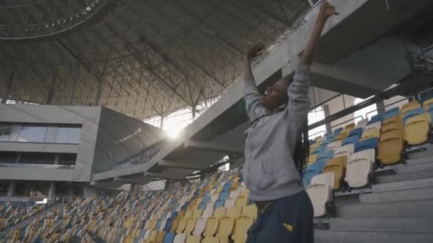 Nettes schwarzes afrikanisches Mädchen, das mit weißen Kopfhörern im Fußballstadion tanzt und Musik hört. Freiheitsbegriff Freude — Stockvideo
