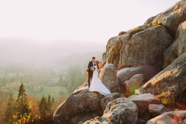 Arka plan olarak kırsal manzaralı görkemli kayalık dağ uçurumun günbatımı ışıkları Romantik yeni evli çift