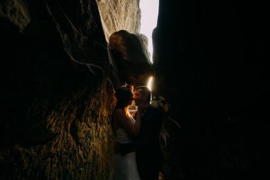 Romantik güzel gelin ve koyu kaya yarık öpüşme zarif şık damat gün batımı parlayan tarafından arka planda