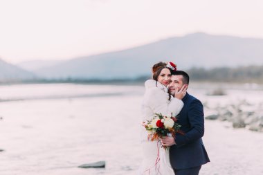 Dağ nehri kıyısındaki çakıl taşı plajında poz veren çekici gelin çifti.