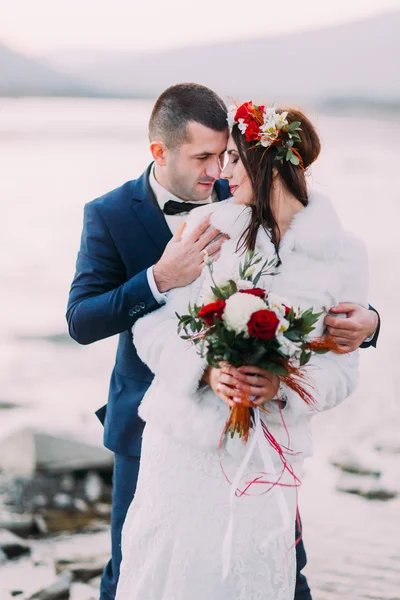 Glückliches Brautpaar hält sich am Kieselufer mit Waldhügeln als Hintergrund — Stockfoto
