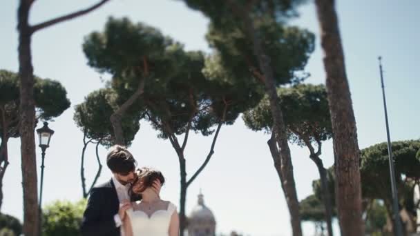 Pareja de boda bajo cielo azul claro en la plaza pública de Roma, Italia. Elegante novio tendelrly besar con hermosa novia. Luna de miel en Italia, Europa — Vídeo de stock