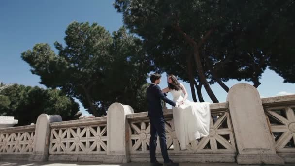 Coppia di sposi sul romantico ponte di pietra sul Tevere a Roma. Elegante sposo baciare con bella sposa. Luna di miele in Italia, Europa — Video Stock