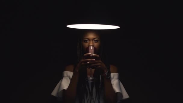 Misteriosa modelo femenina afroamericana sexy bebiendo una copa de vino tinto en fondo de estudio negro en cámara lenta — Vídeos de Stock