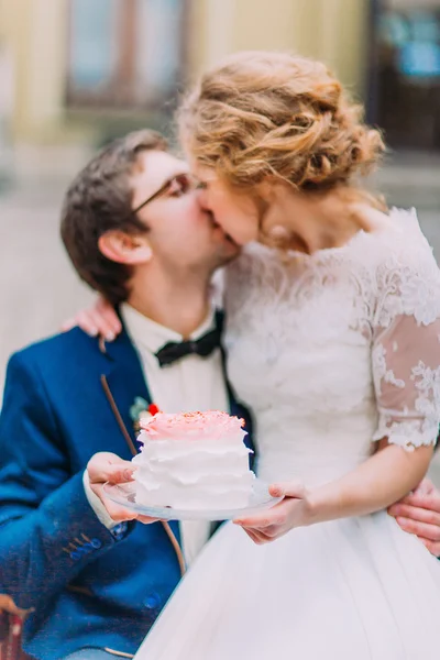 Glückliche Brautpaare küssen sich sanft und halten ihre Hochzeitstorte — Stockfoto