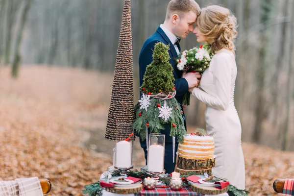 Casal jovem feliz suavemente de mãos dadas perto da mesa decorada para férias de Natal na floresta de outono . — Fotografia de Stock