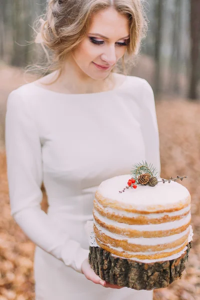 Attraktive blonde Braut mit Hochzeitstorte im herbstlichen Wald — Stockfoto