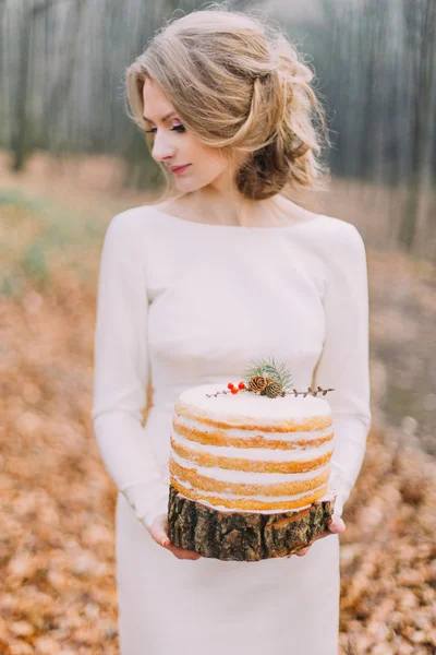 Attraktiv blond brud med bröllopstårta i skogen höst — Stockfoto