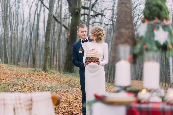 Happy young wedding couple walking and hugging near the decorated table for Christmas holidays in autumn forest.