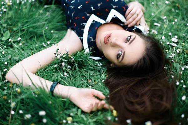 Retrato de close-up de jovem mulher bonita em vestido bonito deitado na grama com flores ao redor. Vista superior — Fotografia de Stock