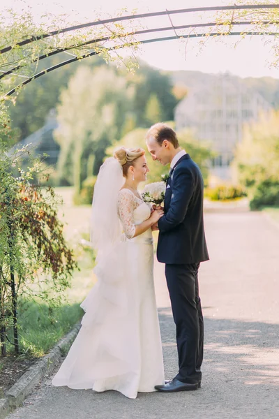 Hermoso novio joven y novia mirando el uno al otro en el día de la boda. Soleado parque de verano en el fondo —  Fotos de Stock