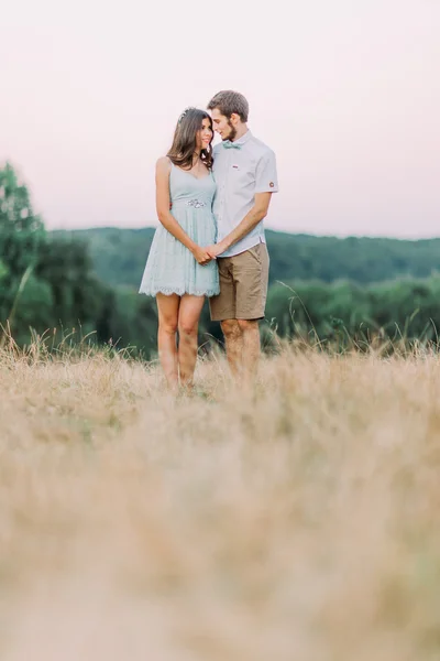 Joven pareja feliz y elegante de pie en el campo de verano. Bosque verde sobre fondo —  Fotos de Stock