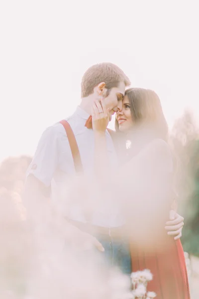 Ritratto sensuale all'aperto di una giovane coppia di moda elegante che si abbraccia nel campo estivo. Fiori d'erba in primo piano — Foto Stock