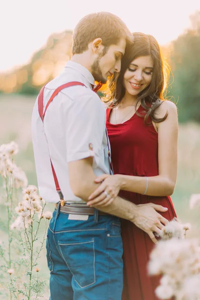 Atractiva joven feliz pareja abrazándose en el hermoso campo de verano al atardecer — Foto de Stock