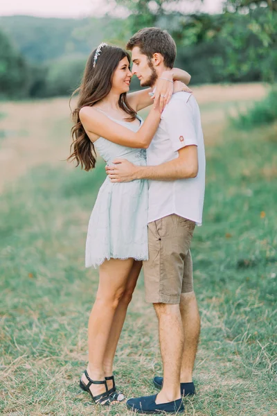 Hermosa pareja joven con amor se miran el uno al otro y abrazándose en el prado verde. Vista trasera. Maravilloso día verano — Foto de Stock