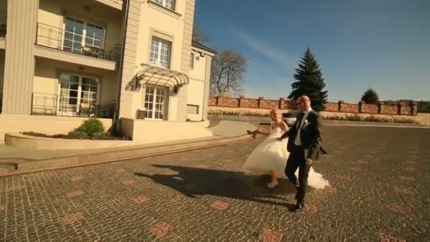 Gelukkige bruid en bruidegom lopen samen bij het hotelgebouw op hun trouwdag — Stockvideo