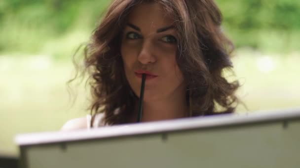 Close-up of beautiful dreamy brunette woman artist with pencil in hands painting the picture outdoor in the forest — Stock Video