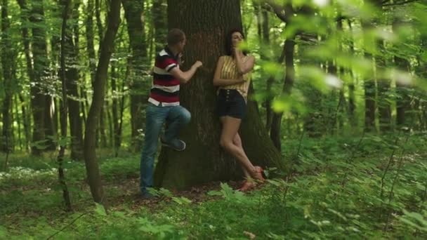 Young happy couple carving a heart with their initials on a tree. Green spring forest background — Stock Video