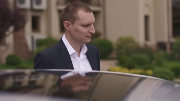 Elegante novio elegante de pie cerca de su coche en el fondo de la ciudad vieja — Vídeos de Stock