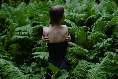 Ferns ormanda arasında oturan çıplak omuz ile güzel bir genç kadının arkadan görünüş