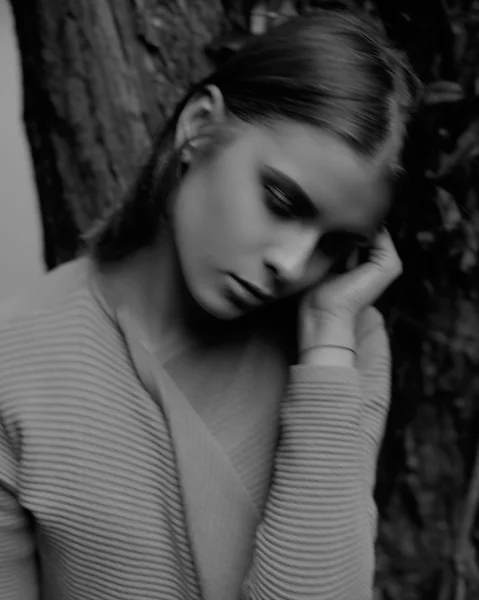 Black and white portrait of beautiful young woman holding hand in hair with closed eyes while leaning at the tree — Stock Photo, Image