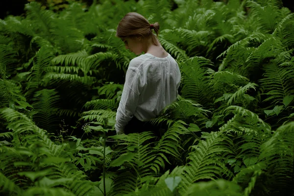 Hermosa mujer posando mirando hacia abajo entre helechos en el bosque. Fantasía y surrealismo — Foto de Stock
