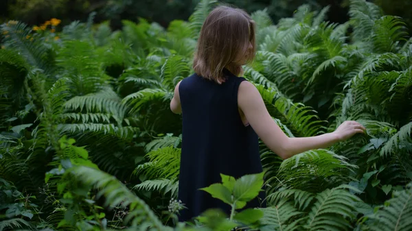 Visão traseira da jovem explorando uma floresta com samambaias verdes — Fotografia de Stock