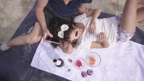 Encantadora pareja rica en un picnic relajándose con vino y dulces en la playa. Día caliente de verano — Vídeo de stock