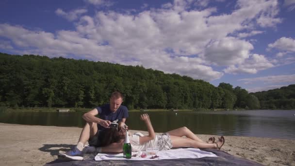 Concept de vie de luxe. Gros plan d'un couple d'amoureux heureux lors d'un pique-nique relaxant et amusant avec du vin et des bonbons sur la plage lors d'une chaude journée d'été — Video