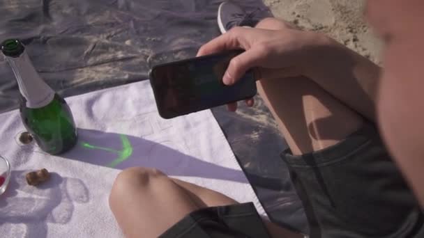 Linda pareja en un picnic relajando la playa en el caluroso día de verano hasta que el hombre comienza a enviar mensajes de texto por teléfono y su novia se enoja y se quita el teléfono inteligente — Vídeos de Stock