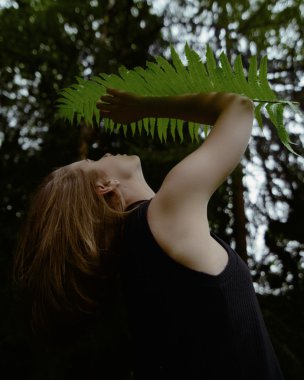 Calm young woman in shade of fern leaf, close-up view from below clipart