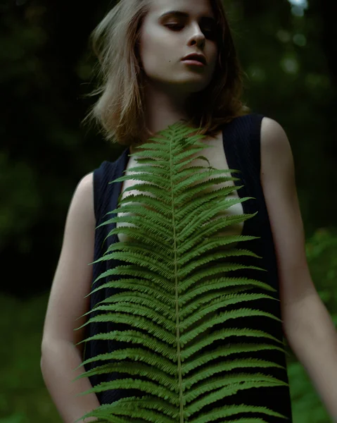 Primer plano de la mujer con vestido negro sosteniendo hoja de helecho verde en el bosque — Foto de Stock