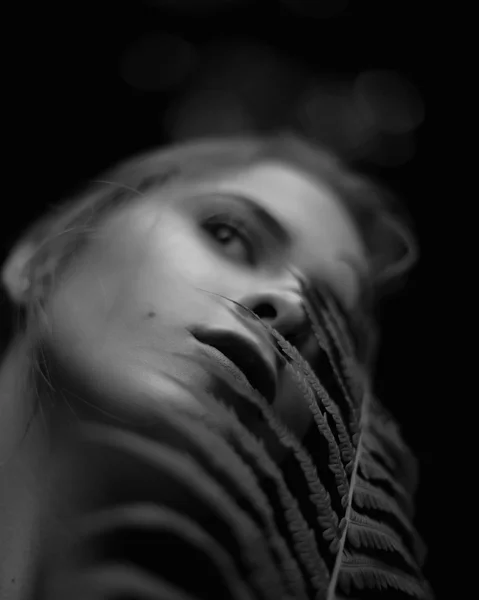 Black and white close-up portrait of young woman holding fern leaf near face — Stock Photo, Image