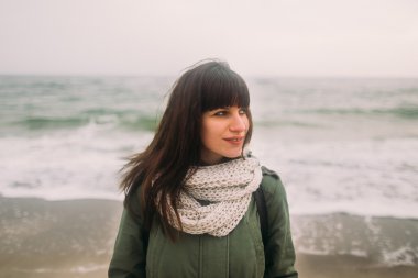 Parka giyen ve soğuk rüzgarlı havalarda deniz kenarında poz forelock ile şık esmer kız Açık kış moda portre.