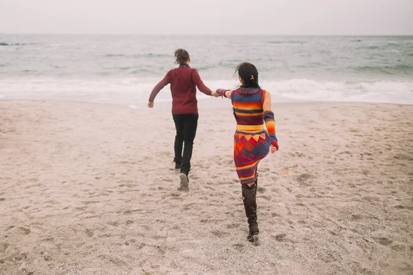 Досить молода стильна пара, що ходить на пляжі в зимовий час. Чоловік веде за руку свою дівчину до моря. Вид ззаду — стокове фото