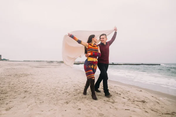 Attractive young happy couple wrapped in white blanket walking on the winter beach and looking at each other. Vintage concept — Stock Photo, Image