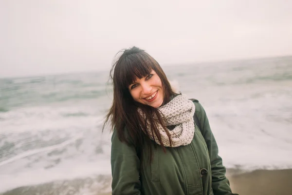 Retrato de moda de inverno ao ar livre da menina morena elegante com o forelock vestindo parka e posando à beira-mar em tempo vento frio . — Fotografia de Stock