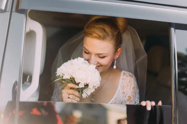 Happy beautiful blonde bride sniffs flowers in the car