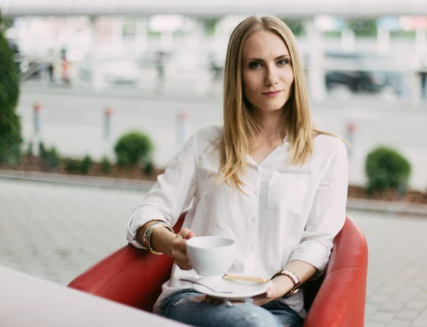 Mujer rubia joven confiada en camisa blanca mirando a la cámara sosteniendo la taza de café — Foto de Stock