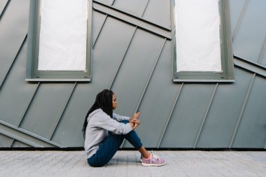 Müzik dinlerken oturan kulaklıklı çekici Afro-Amerikan kadının yan görünümü