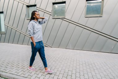 Şehirde kulaklıkla yürüyen gülümseyen afro-Amerikan bir kadının yan portresi