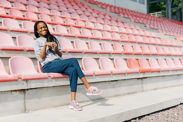 Modelo de mulher bonita afro-americana rir com os olhos fechados na frente de bancos de estádio moderno — Fotografia de Stock