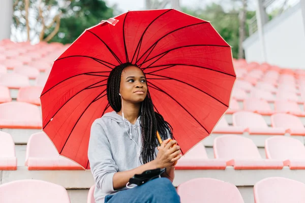 Mulher pensativa sentada no estádio e ouvindo música olhando para cima depois de fazer exercício — Fotografia de Stock