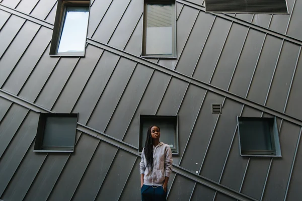 Estilo de vida y foto conceptual de moda de niña afroamericana posando en la pared de metal plateado en ropa deportiva gris con auriculares — Foto de Stock