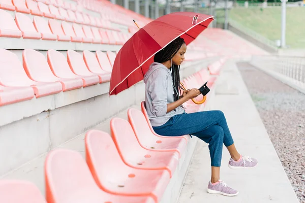 Vista lateral da jovem mulher afro-americana de sportswear azul e cinza ouvindo música no estádio — Fotografia de Stock