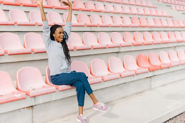 Ευτυχισμένη αφρικανική Αμερικανίδα που ζητωκραυγάζει για την επιτυχία με τα χέρια πάνω από τη θέα ενός σταδίου — Φωτογραφία Αρχείου